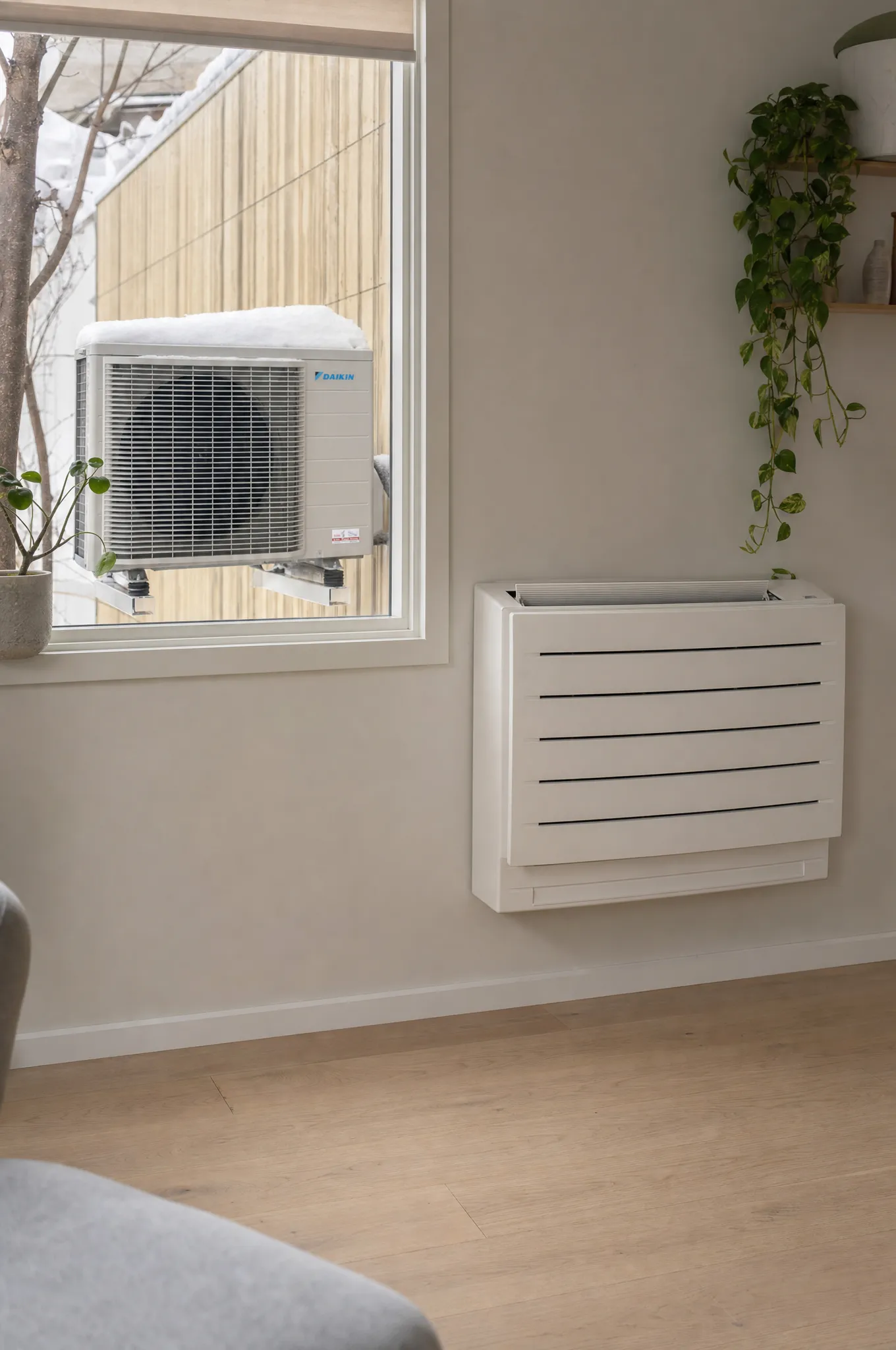 Daikin gulvmodell under vinduet, med utedelen montert på trehusveggen utenfor